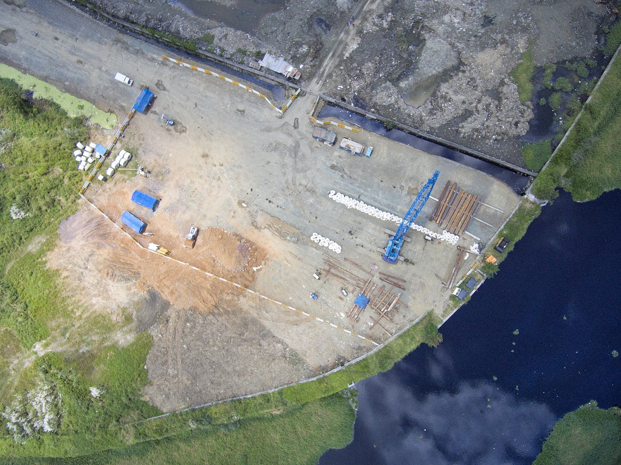 High-angle shot of construction site by a river in the Philippines, featuring cranes and machinery.