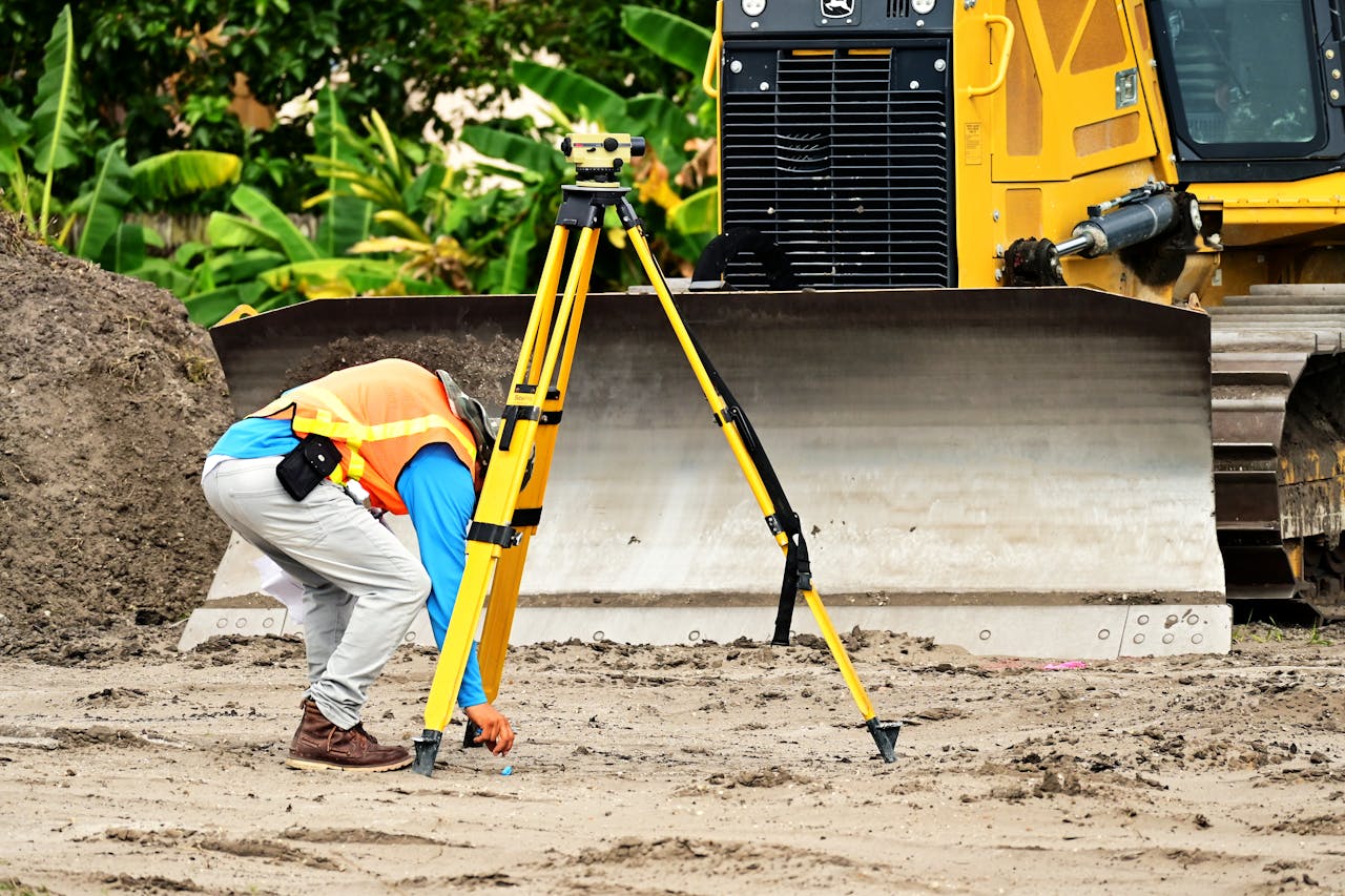 about-us A construction worker operates a total station in front of a bulldozer on a construction site.
