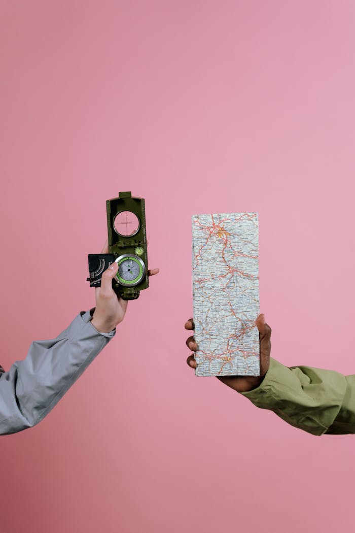 Hands holding a compass and map, symbolizing navigation and direction against a pink backdrop.